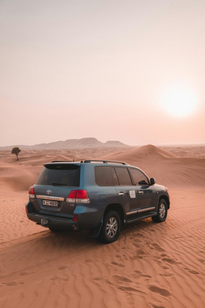 A rugged SUV traverses the sandy dunes of Dubai's desert at sunset, displaying adventure and exploration.